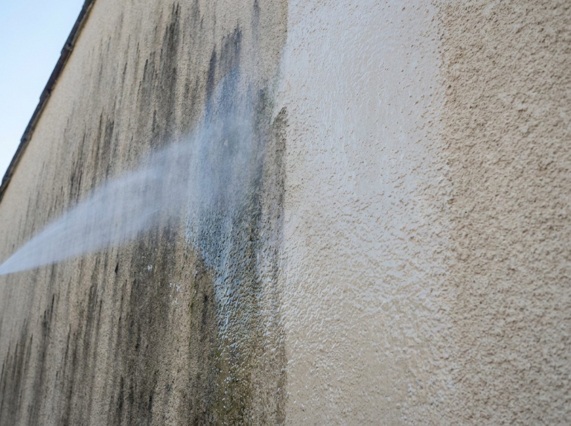 A rendered wall being soft washed, mould streaks lifting away