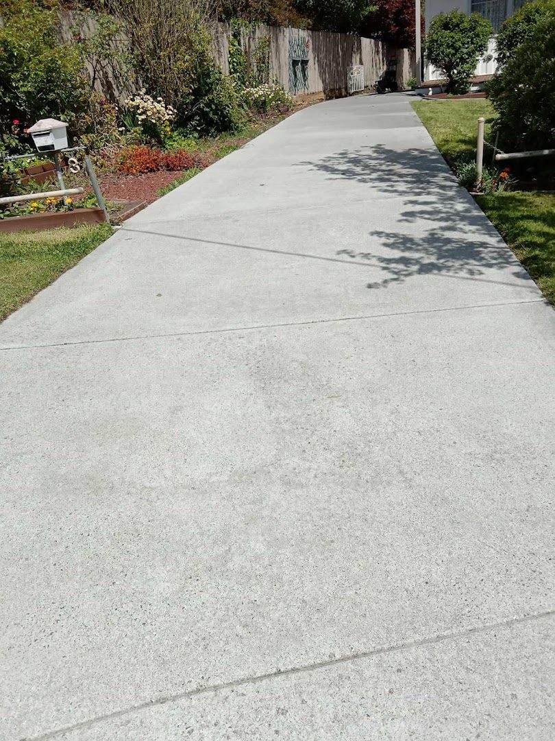A long clean concrete driveway running past a garden bed