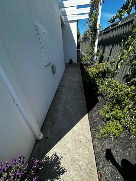 A narrow side path between a house and a fence, photographed before pressure washing