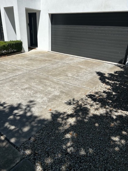 A driveway beside a garage and pebble garden bed, photographed before pressure washing