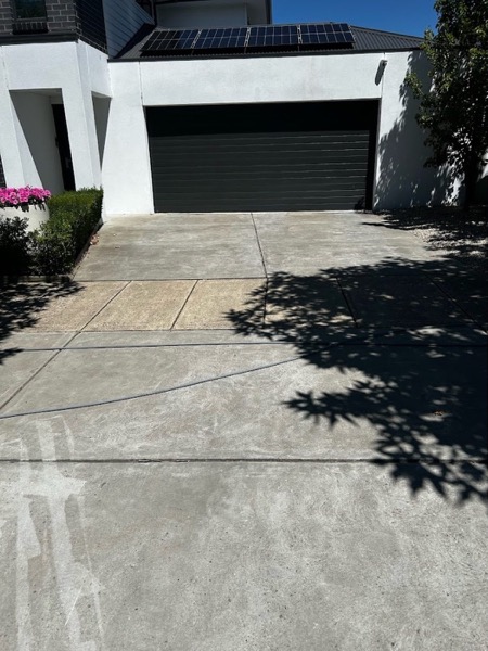 A driveway in front of a rendered home with solar panels, photographed before pressure washing