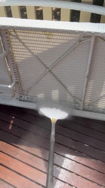 A pressure washer wand spraying a timber deck