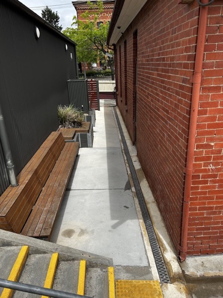 A concrete path and timber bench beside a red brick wall