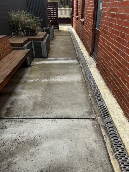 A concrete path beside a red brick wall and a drainage grate