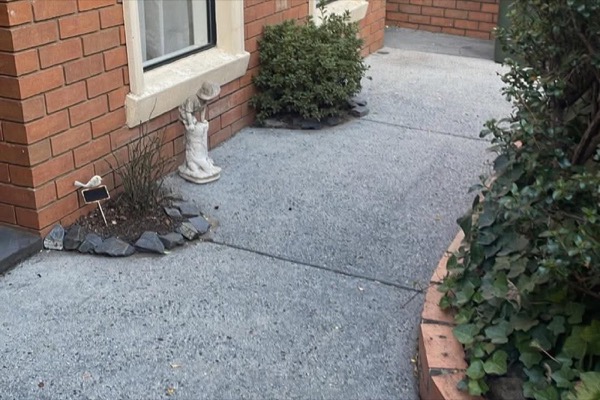 A concrete path beside a red brick house and garden